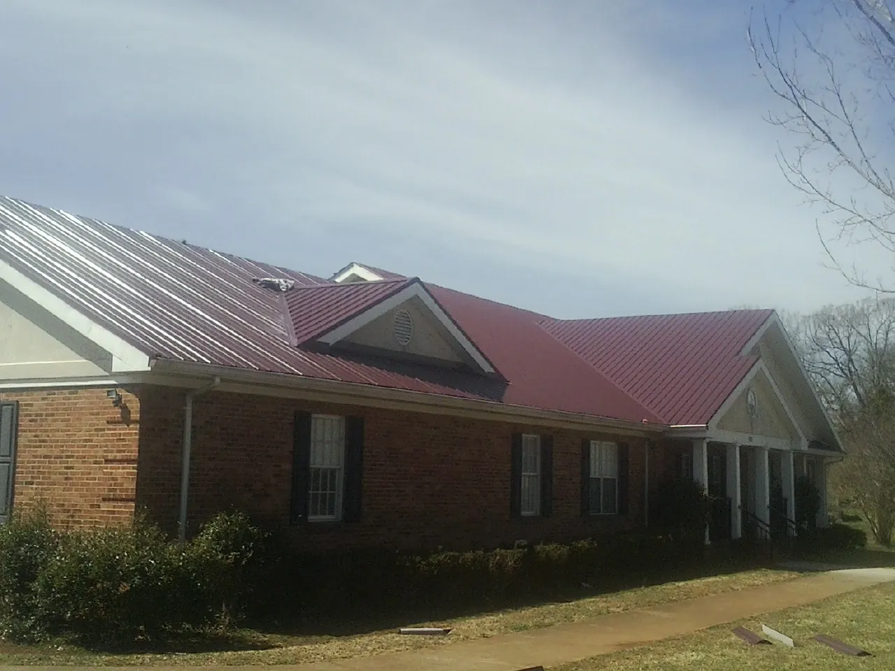 Red metal roof with gabled entries on a long brick building, from a Hail Damage Roof Repair job in Midlothian