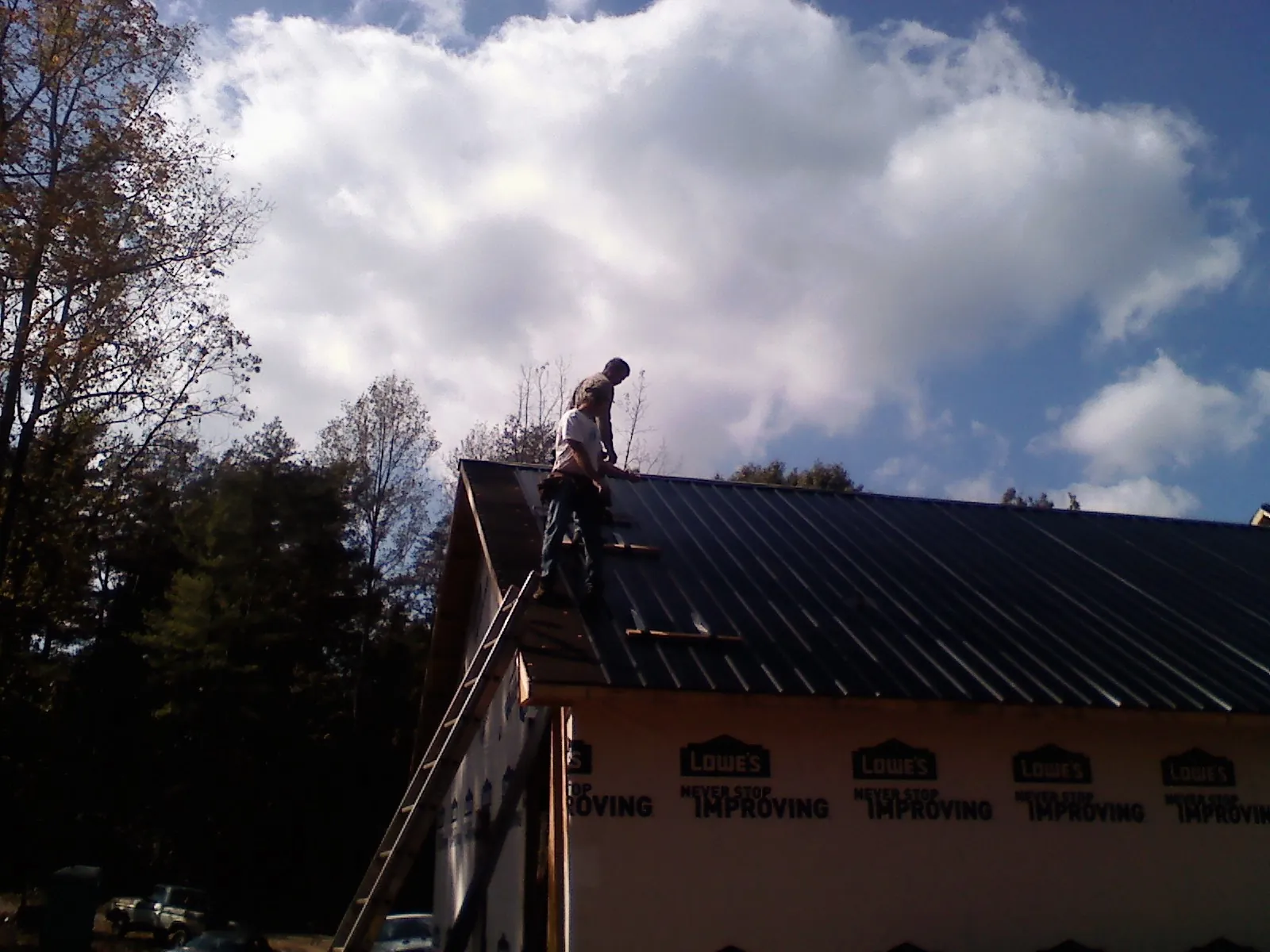 Roofer fastening dark metal panels high against a cloudy sky, from a Roof Inspection job in Midlothian